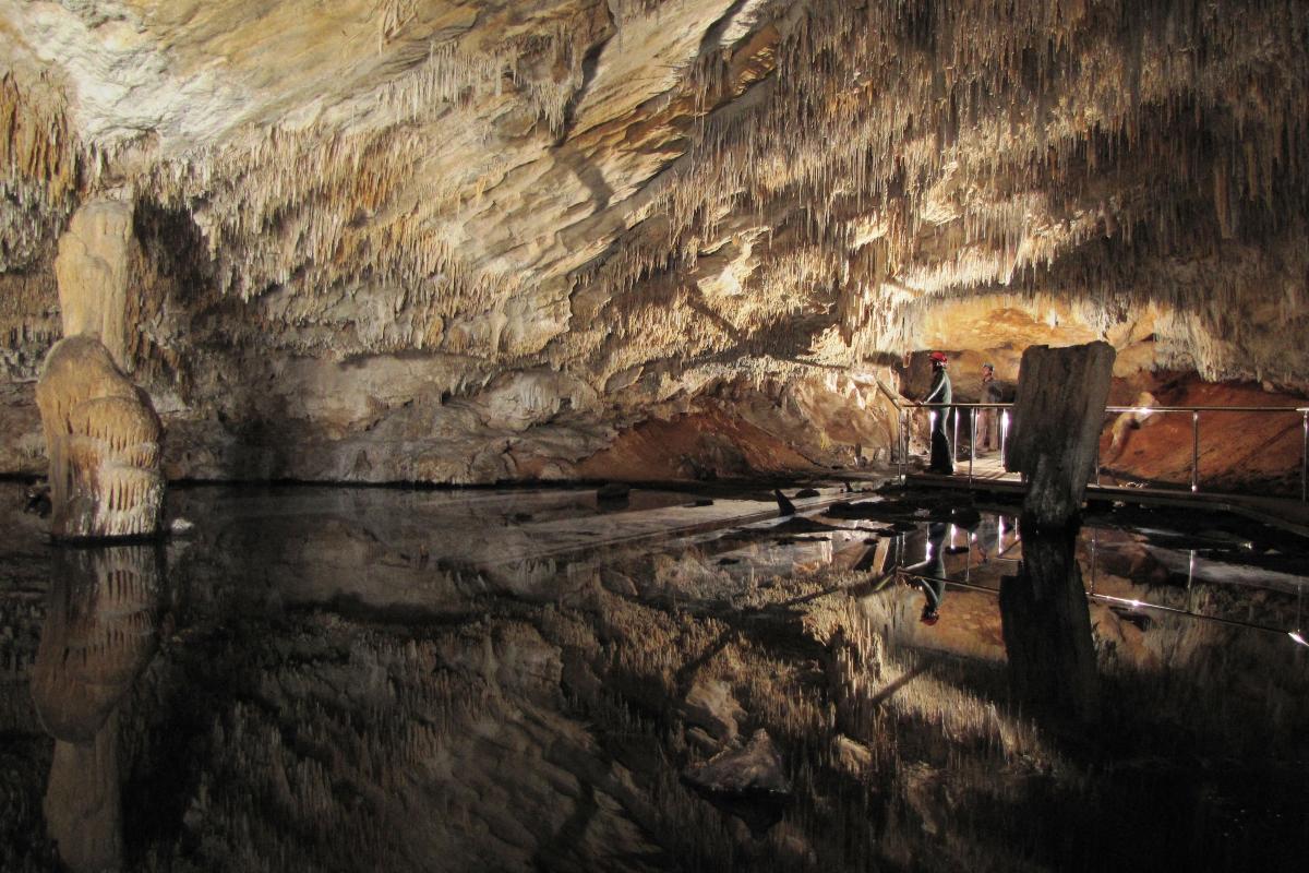 two cavers looking at the reflections of the cave chamber in the pool of water in the cave
