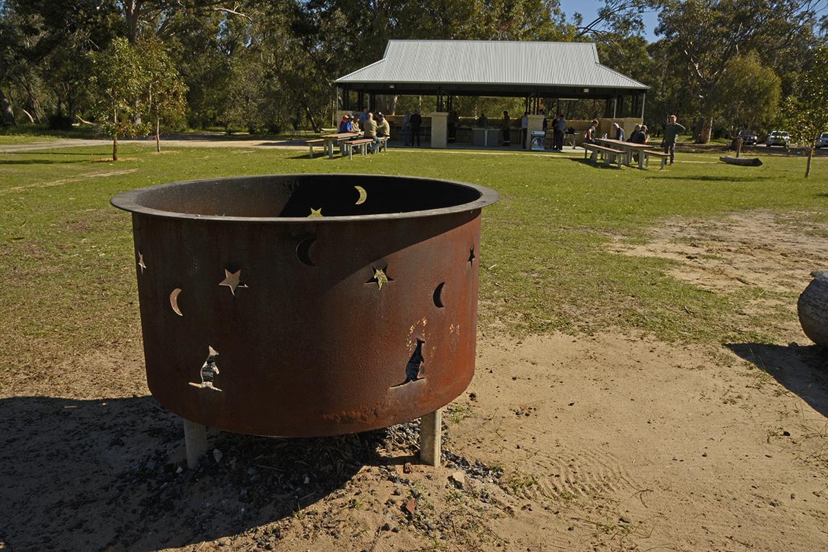 Open grassed area with picnic tables and barbecue shelter and decorative fire pit.