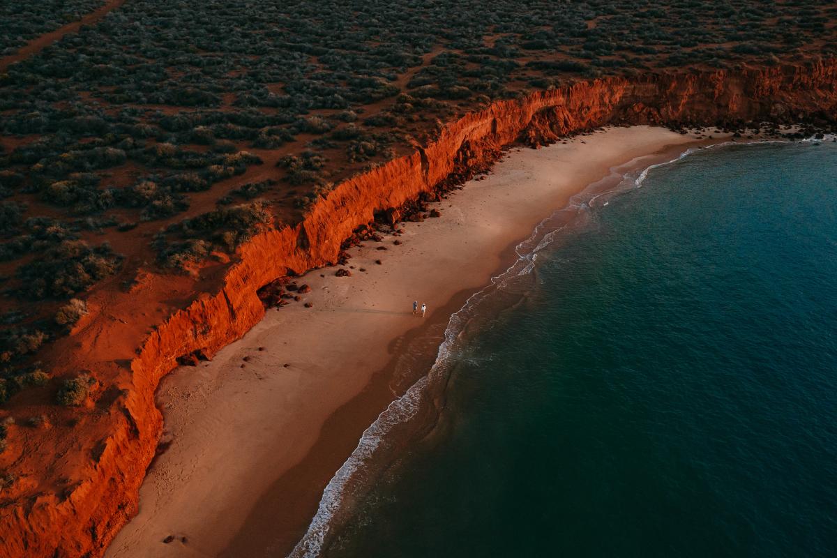 Aerial view looking down coastline of layered rugged red rock and green blue ocean water
