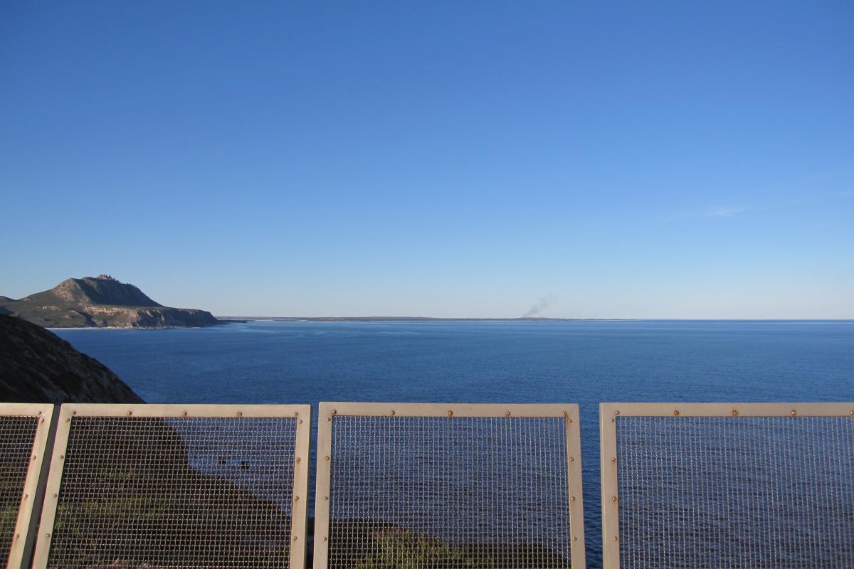 View from a metal viewing platform out across a wide expanse of ocean with rock cliffs on one side
