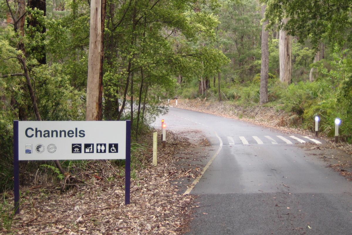 a sign on the left hand side of the bitumen road that winds through the forest