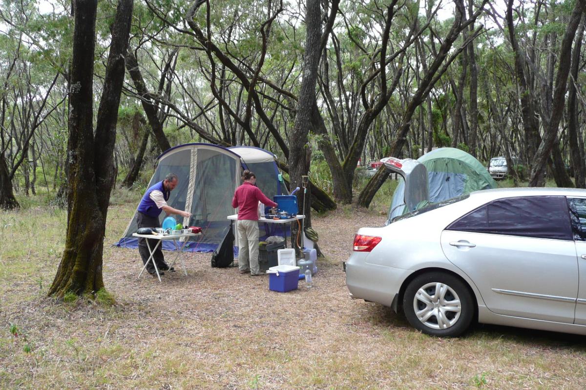 A vehicle and tent with people in a camping area.