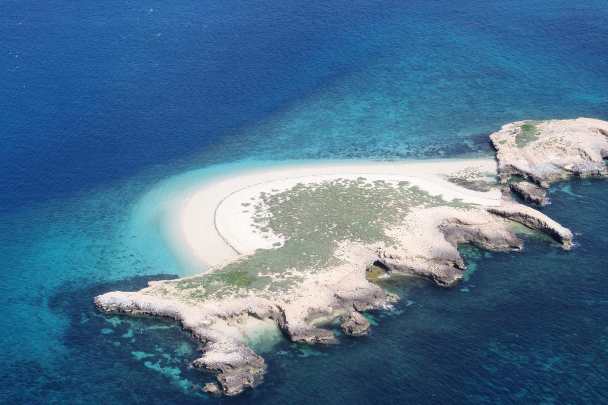 Aerial view of small sandy island surrounded by blue water