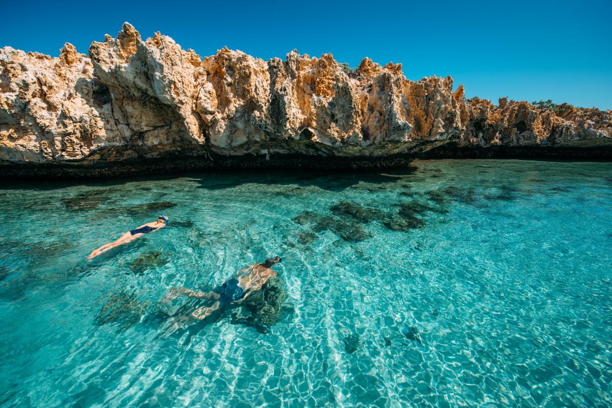 Couple snorkeling near limestone rock in clear green water