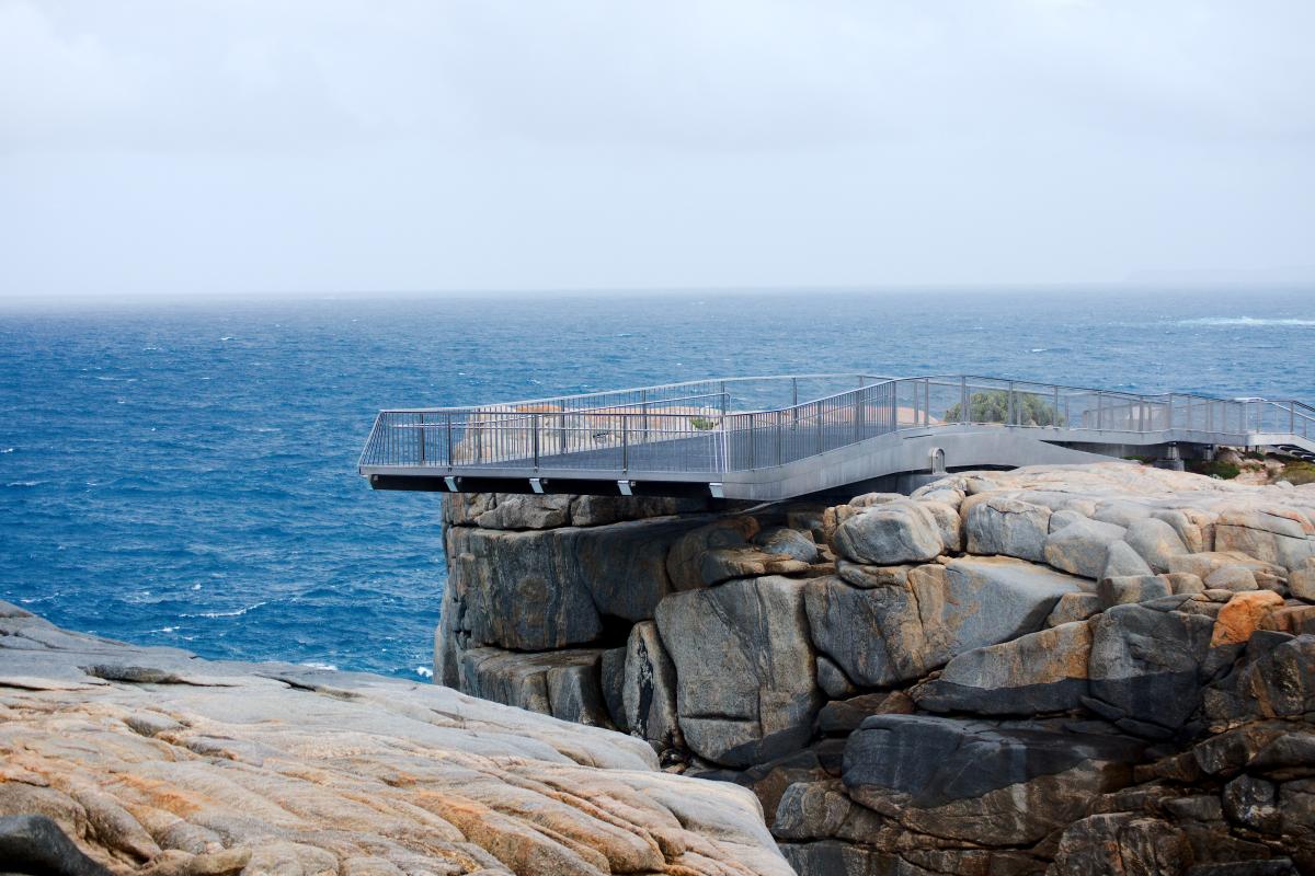 a lookout that is over the edge of the granite with a blue ocean in the background