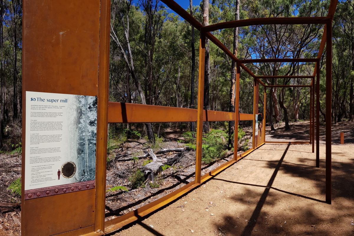 Jarrahdene walk trail at Jarrahdene Campground interpretive sign sharing stories of the historic mill site from within the sculpture