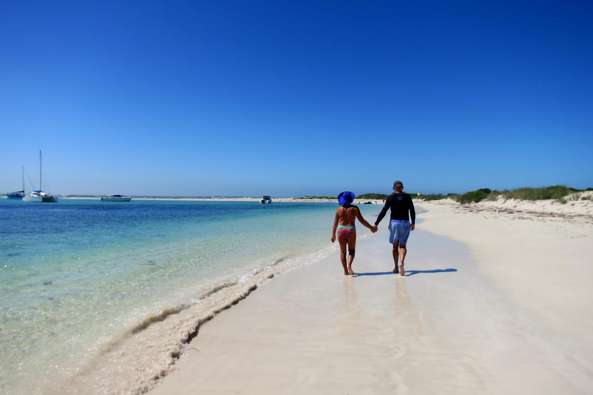 two people holding hands and walking on the white sandy beach next to the ocean.\