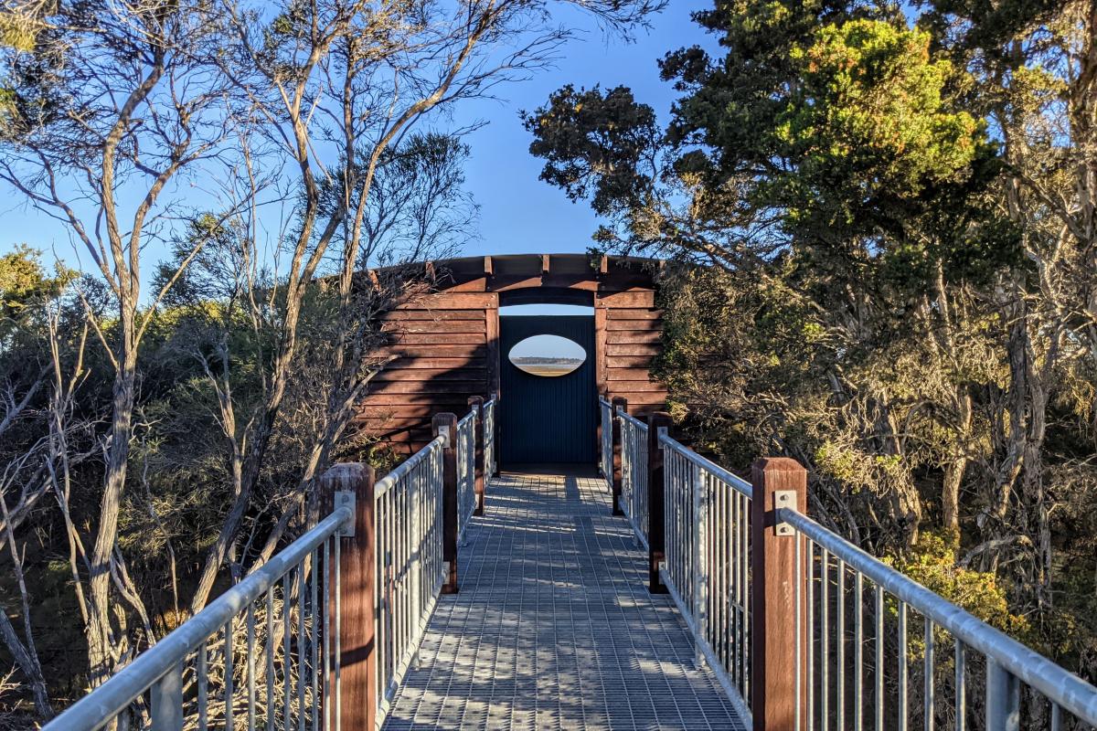 Wooden observatory structure at the end of a metal boardwalk through the bushes