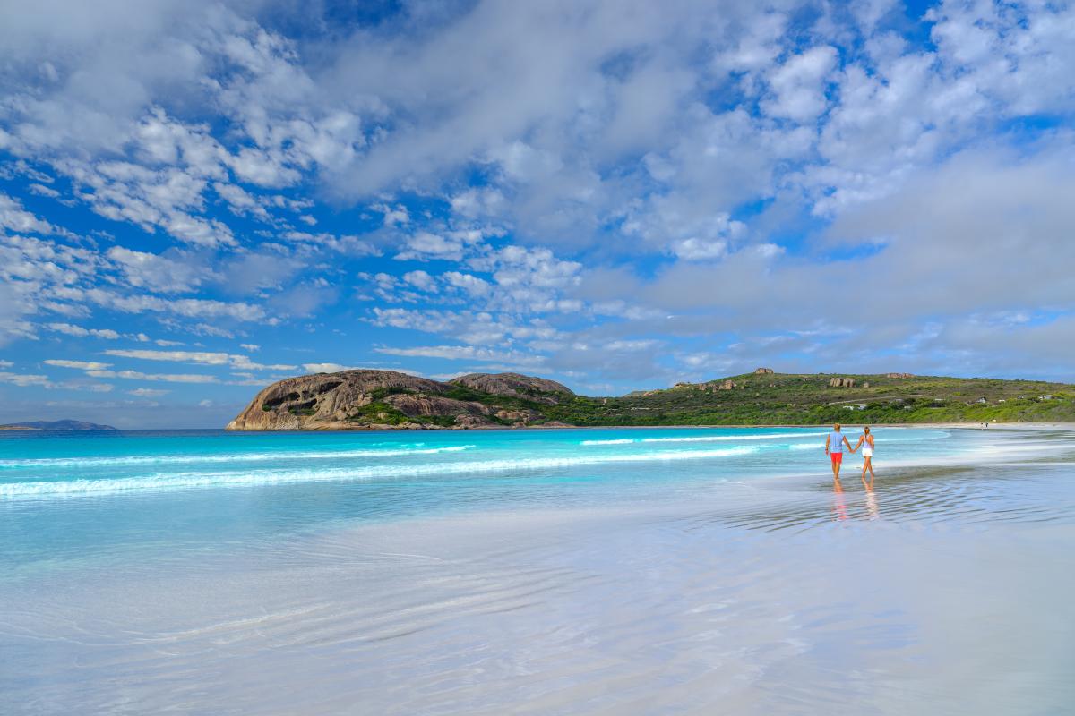 Visitors walking along the wide beach with turquoise water and rocky headland in the distance