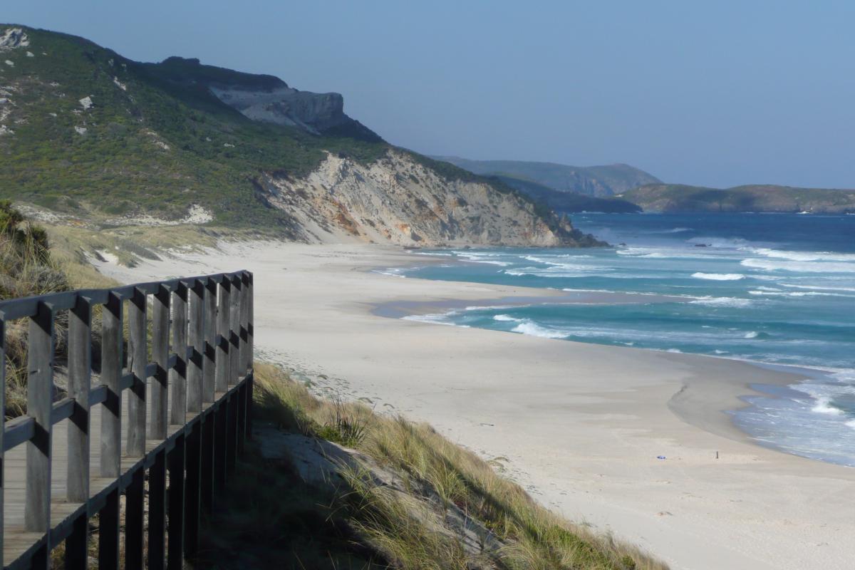 Wooden boardwalk to a white sandy beach with high green hills and blue ocean