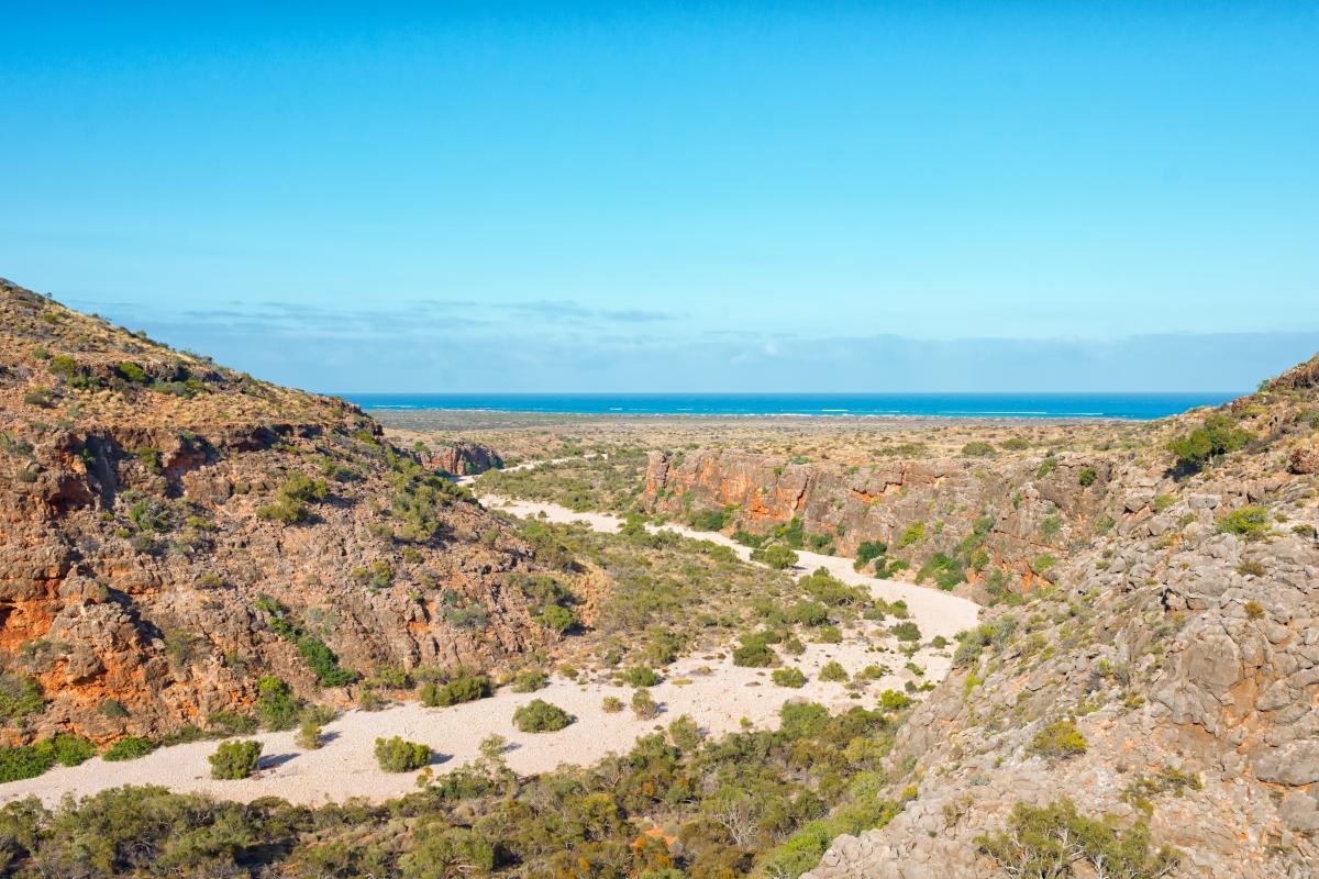 View of dirt track leading out between rock walls to bright blue ocean