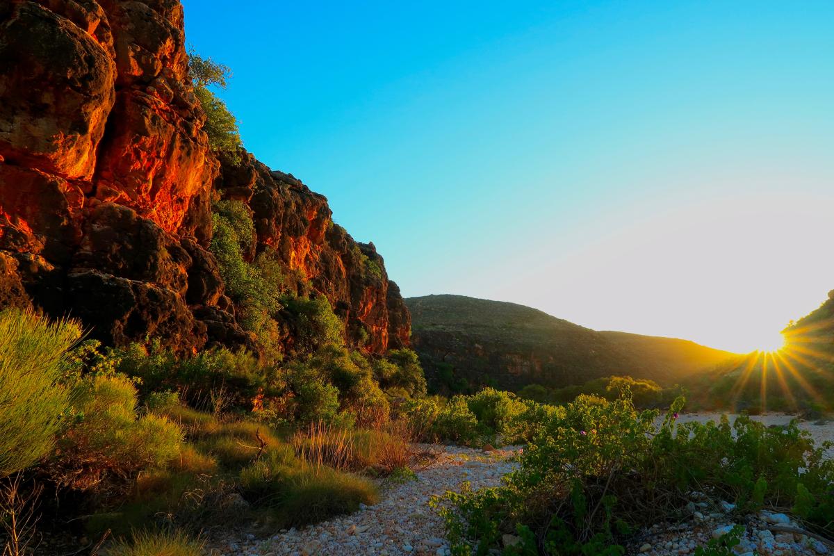 View of sun poking around the edge of a rock wall