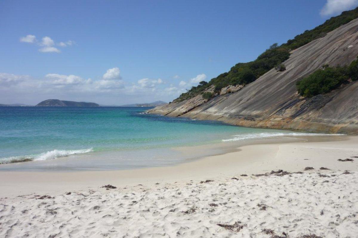 white sandy beach with blue sky and ocean with a hill