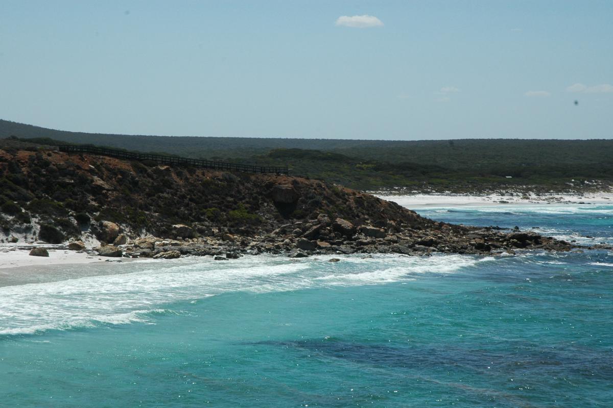 view at Point Ann of waves breaking onto a rocky shore with a sweeping sandy bay in the distance