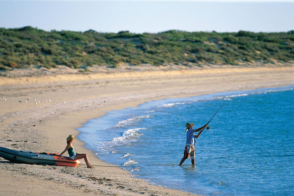 One person fishing and one person watching from the shore