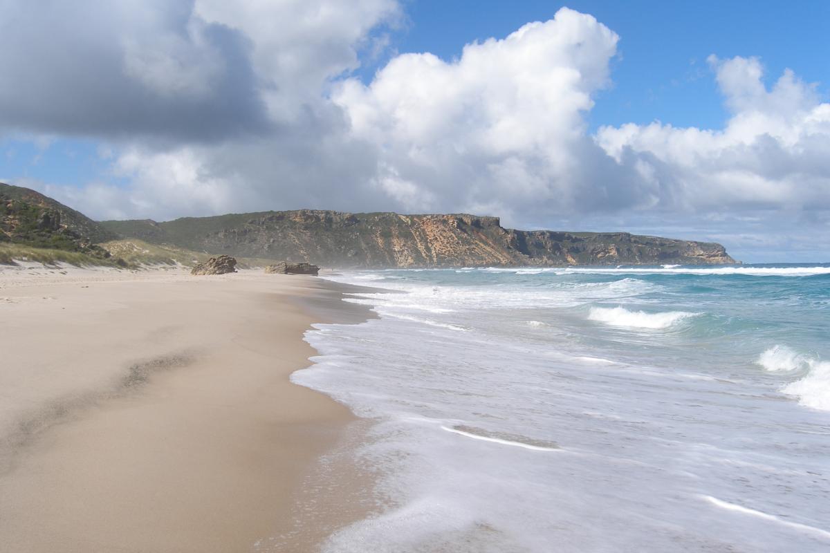 waves and a sandy beach with limestone cliffs in the background