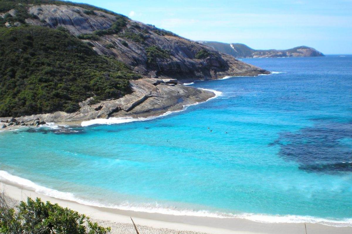 white sandy beach with blue sky and ocean with a hill