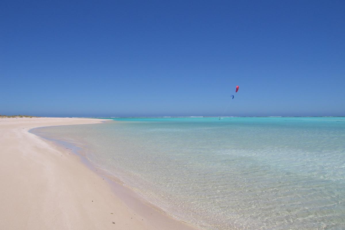 Clear blue water near white sandy beach and kite surfers