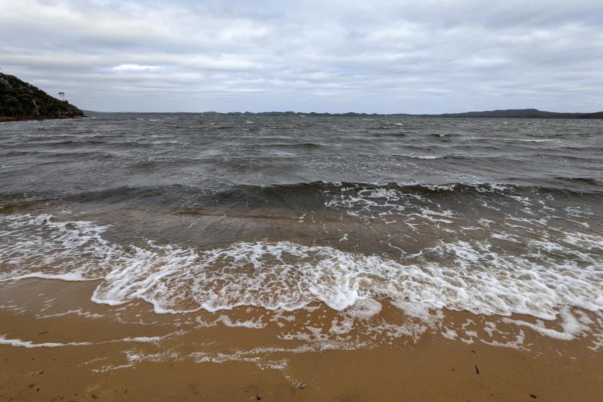 Nornalup Inlet at Sandy Beach with small waves breaking on the shore on an overcast day