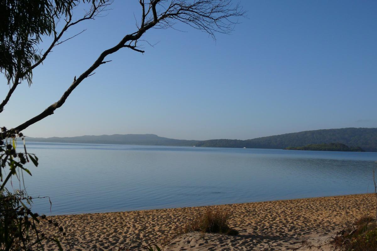 sandy beach of the still waters of the inlet with blue skies and low hills in the distance