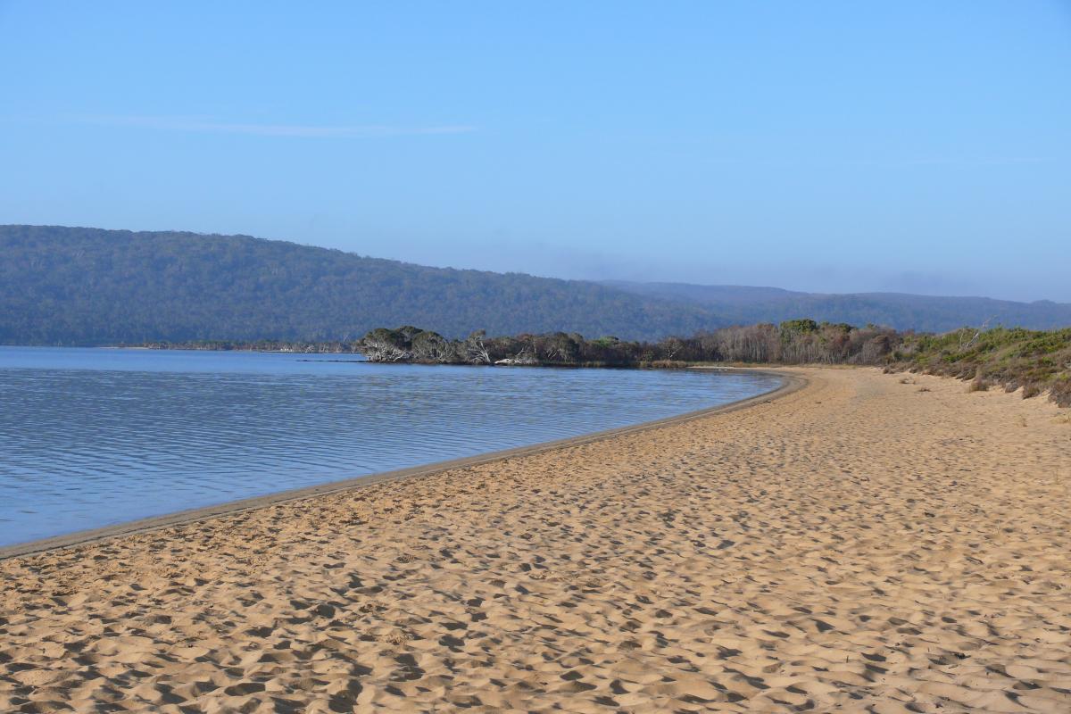 sandy beach of the still waters of the inlet with blue skies and low hills in the distance