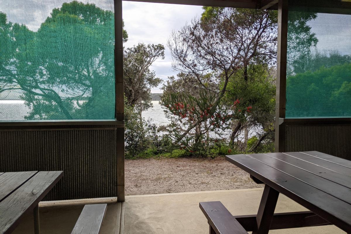 Picnic benches in undercover area with a view of the water at Stokes Inlet