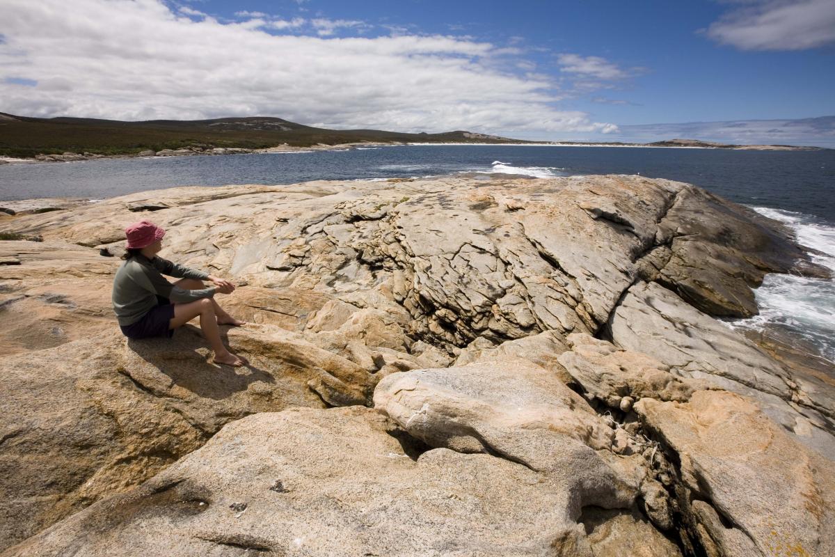 Visitor sitting on granite rocks overlooking the ocean and surrounding white sand bays