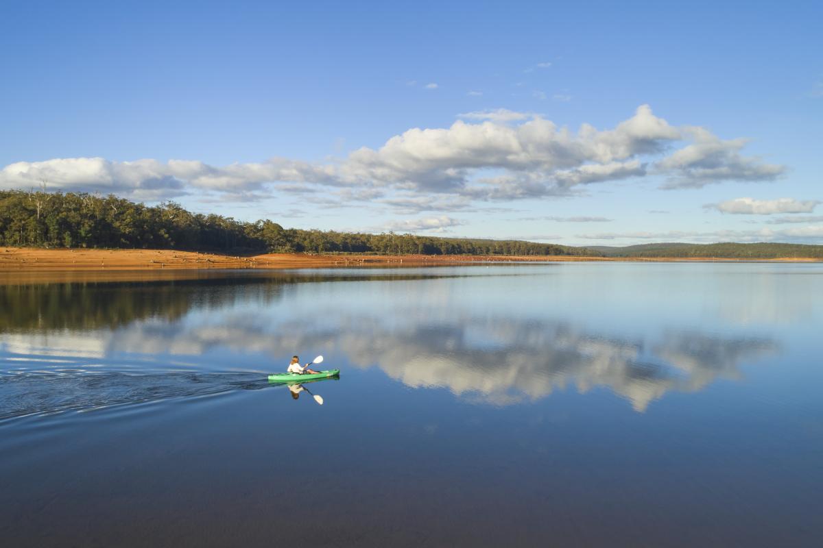 reflections of a blue sky with a few clouds on the still waters of the dam with forest in the background