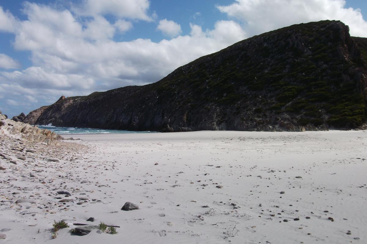 pure white sandy beach with a hill and cloudy blue skies in the background