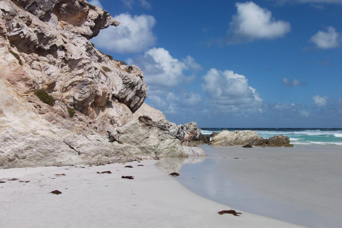 white sandy beach and limestone cliff with cloudy blue sky and ocean