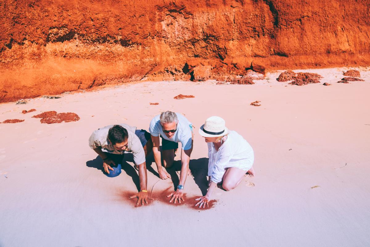 Three people making hand prints in the sand.