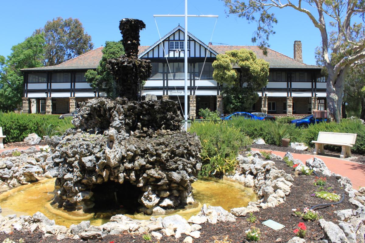 A grand old heritage listed building surrounded by green grass and shaded trees.s