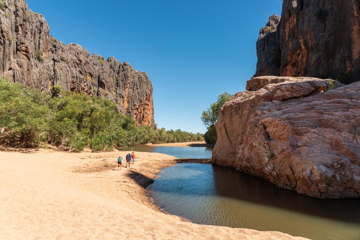 Bandiln͟gan (Windjana Gorge) people walking on the sand beside the freshwater stream with massive rock walls on either side