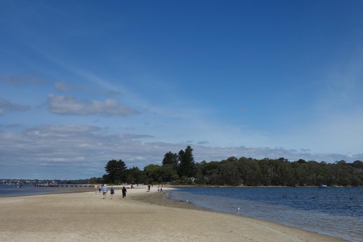 People walking on the sand spit toward shore at low tide.