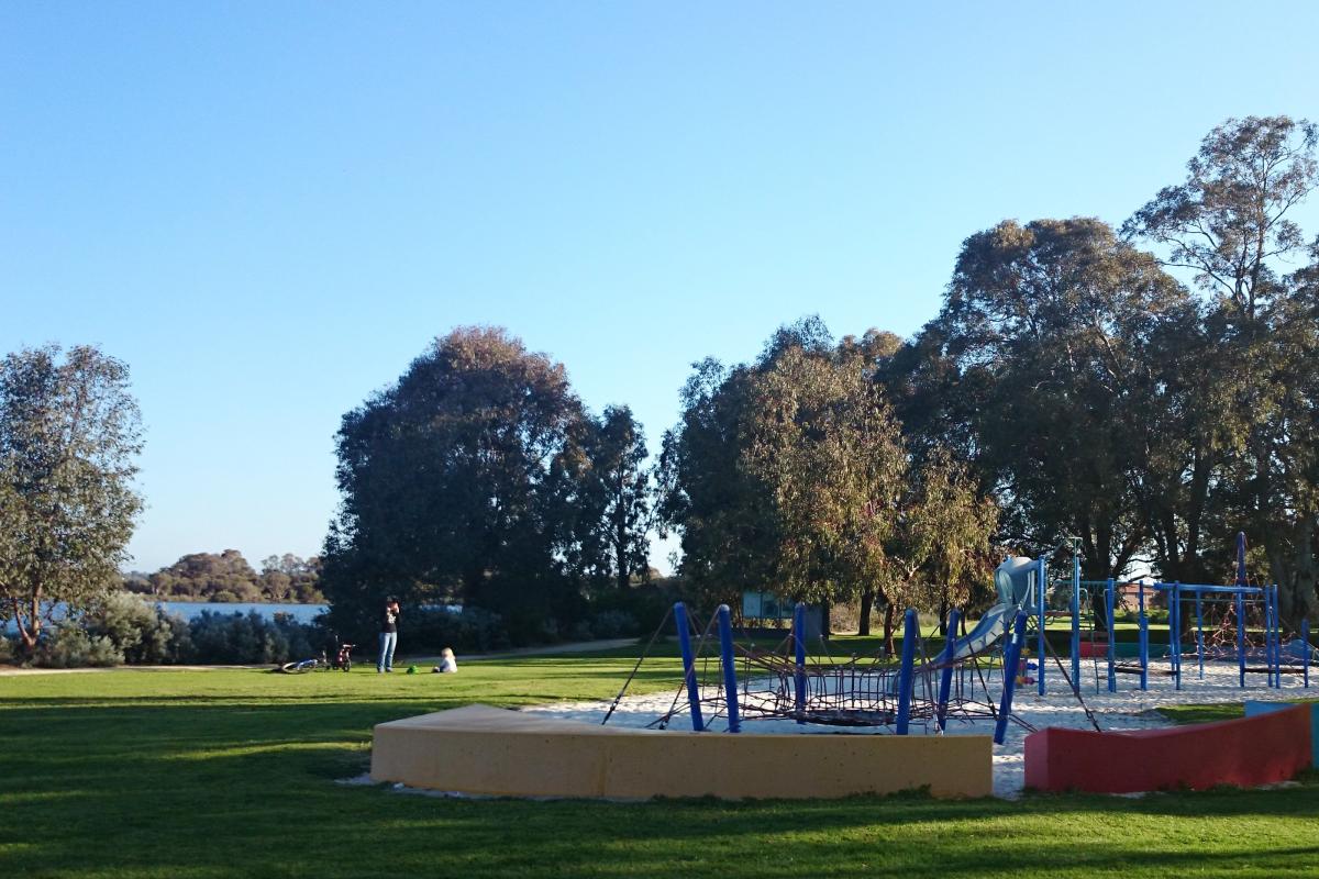 A modern playground is surrounded by a grassed play area near the lake.
