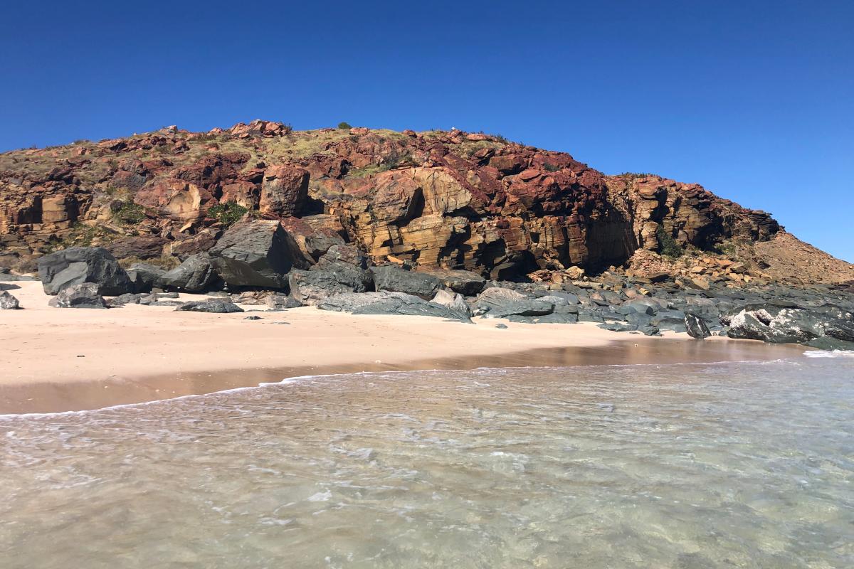 Clear ocean lapping onto a sandy beach at Rosemary Island with jagged rocks rising in the background