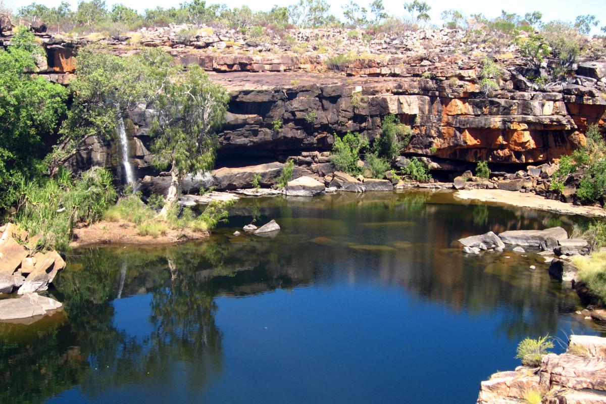 Pool of water with layered rock all round and small water fall