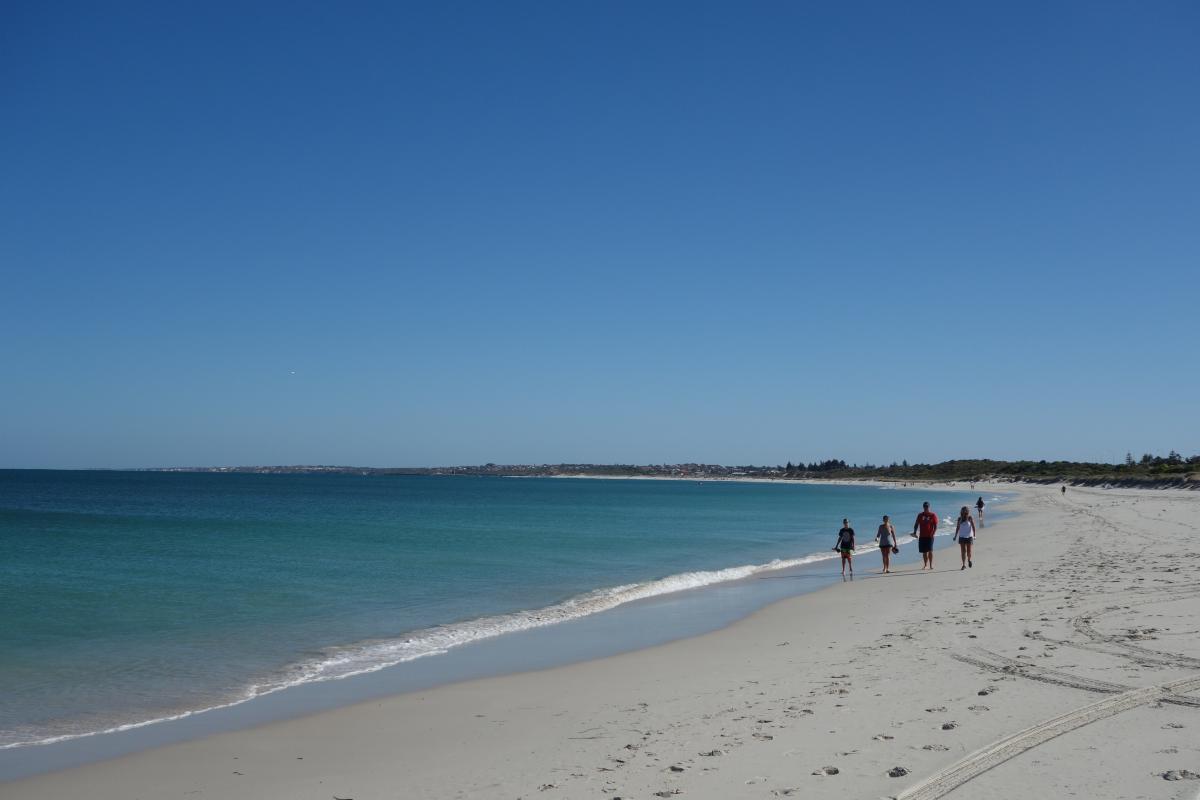 A family walks along the beach in the wash of the waves with shoes in hand.