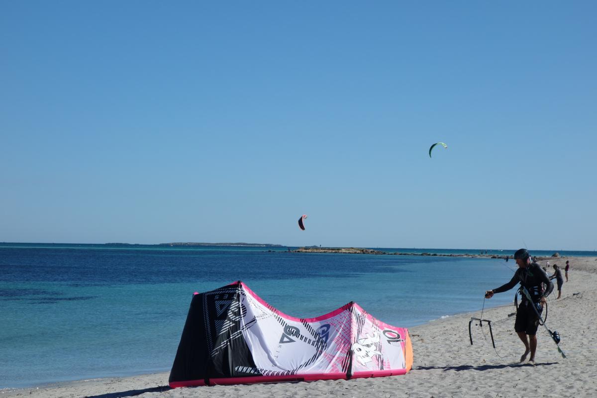 A kite surfer prepares equipment on the sandy beach at Woodman Point.