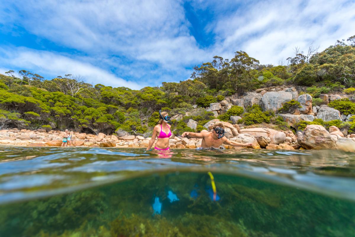 Two people standing in knee deep water wearing snorkel and goggles. 