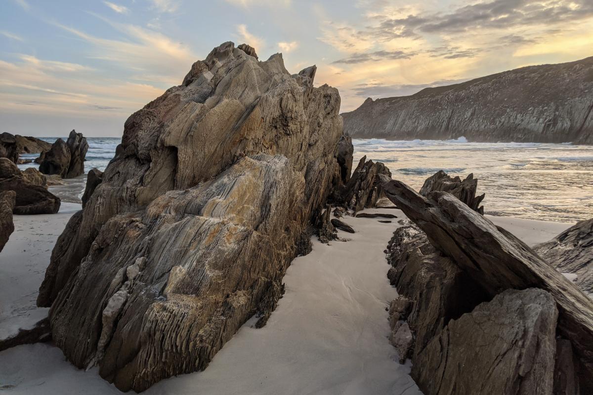 jagged rocks protrude out of the white sands and ocean at Whalebone Cove