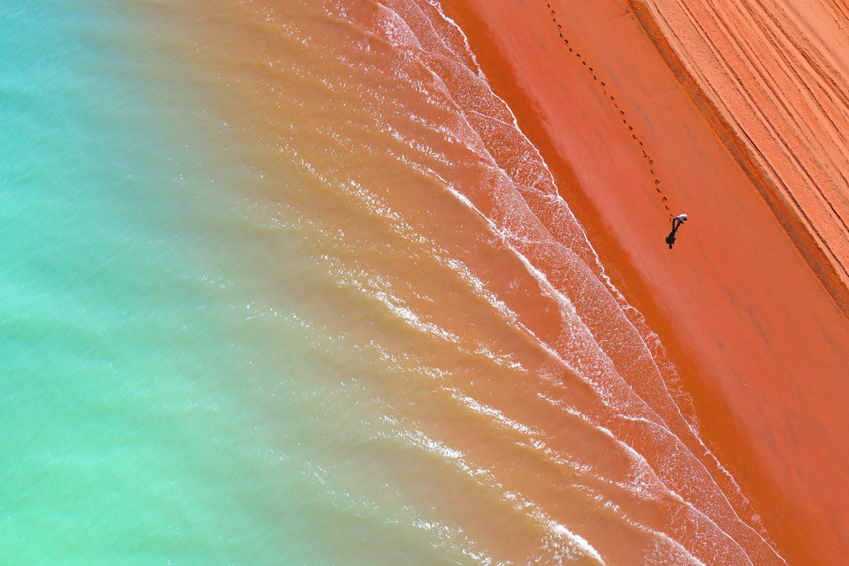 Aerial view of pinda red beach sand next to green waters. 