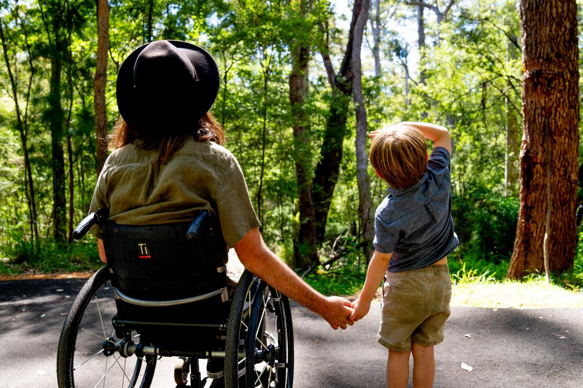 Person in wheelchair holding hands with a child looking at the trees. 