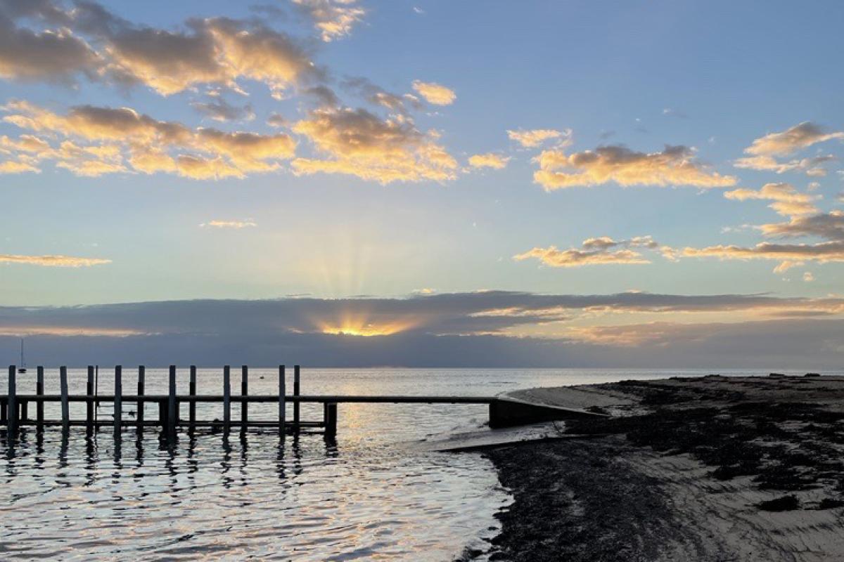 Wooden jetty at the beach at sunset and the sky is blue and yellow. 