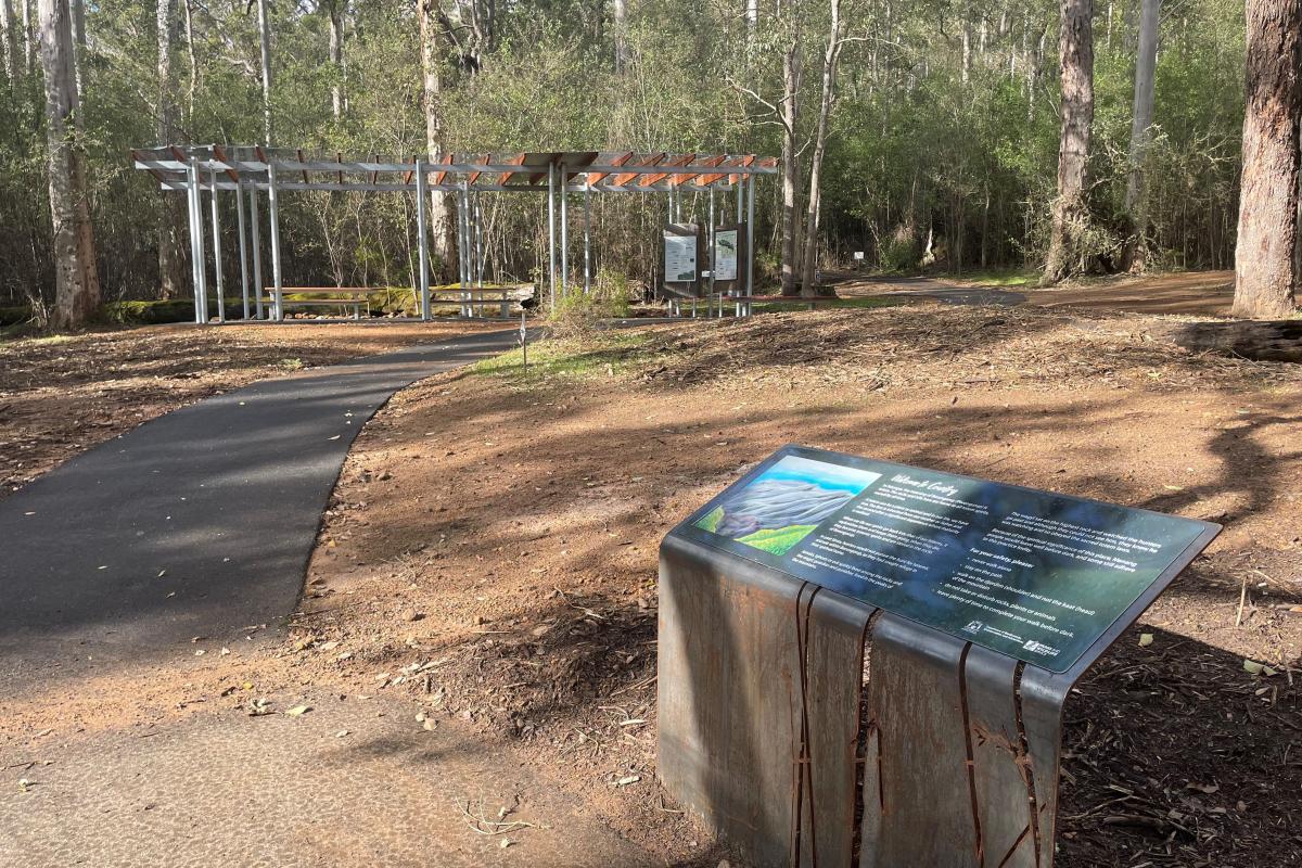 Metal sign near a path leading towards trees in the background.