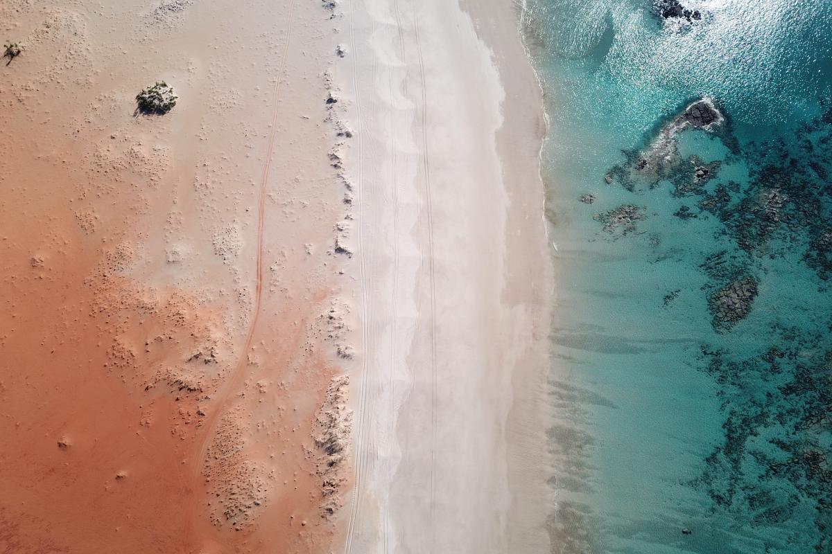 Aerial view showing three colours of red sand, white foam and blue water.