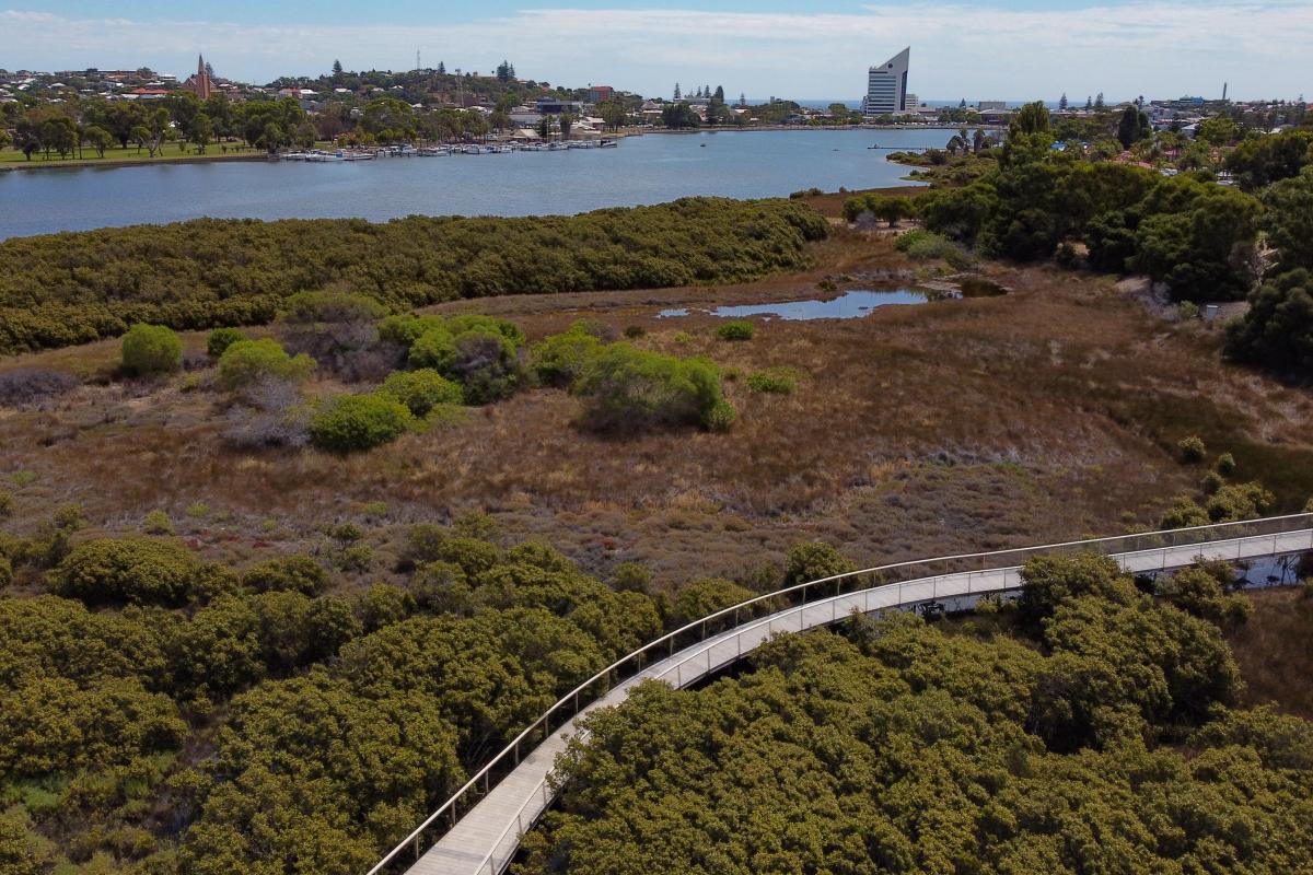 Aerial view looking down on a boardwalk over a wetland and water in the distance. 