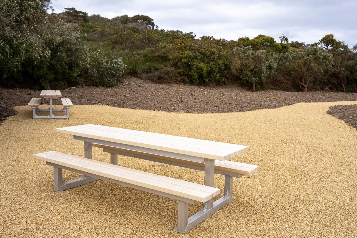 Two picnic benches and tables in a cleared area. 