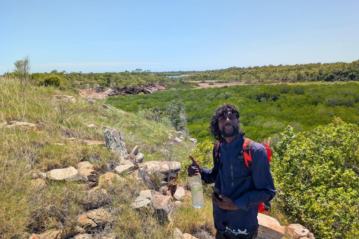 Person standing near a large stone Aboriginal artefact. 