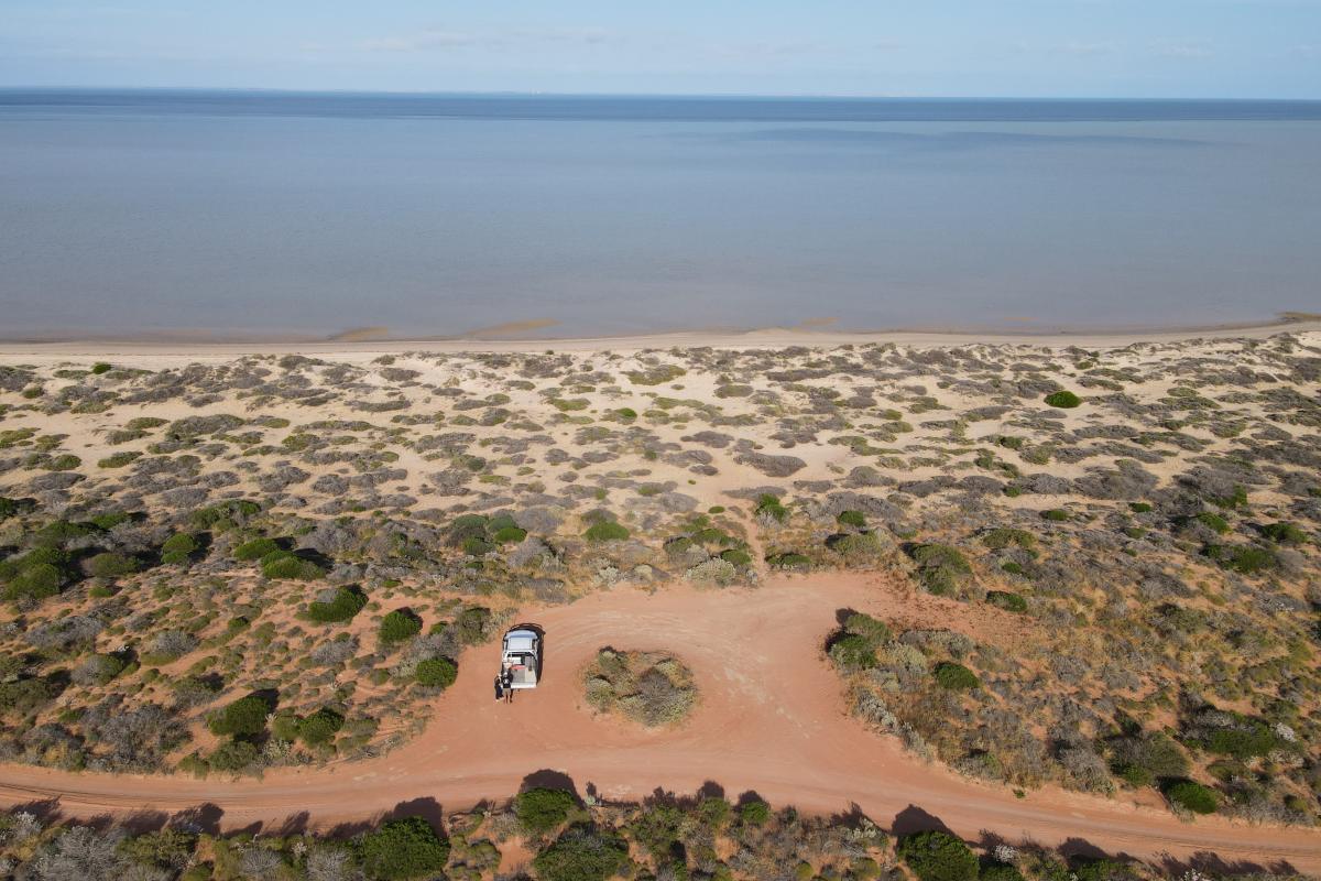 Aerial view of sandy campsite and tracks by the beach. 